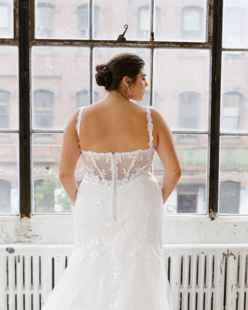 Bride standing looking out of windows in fitted gown